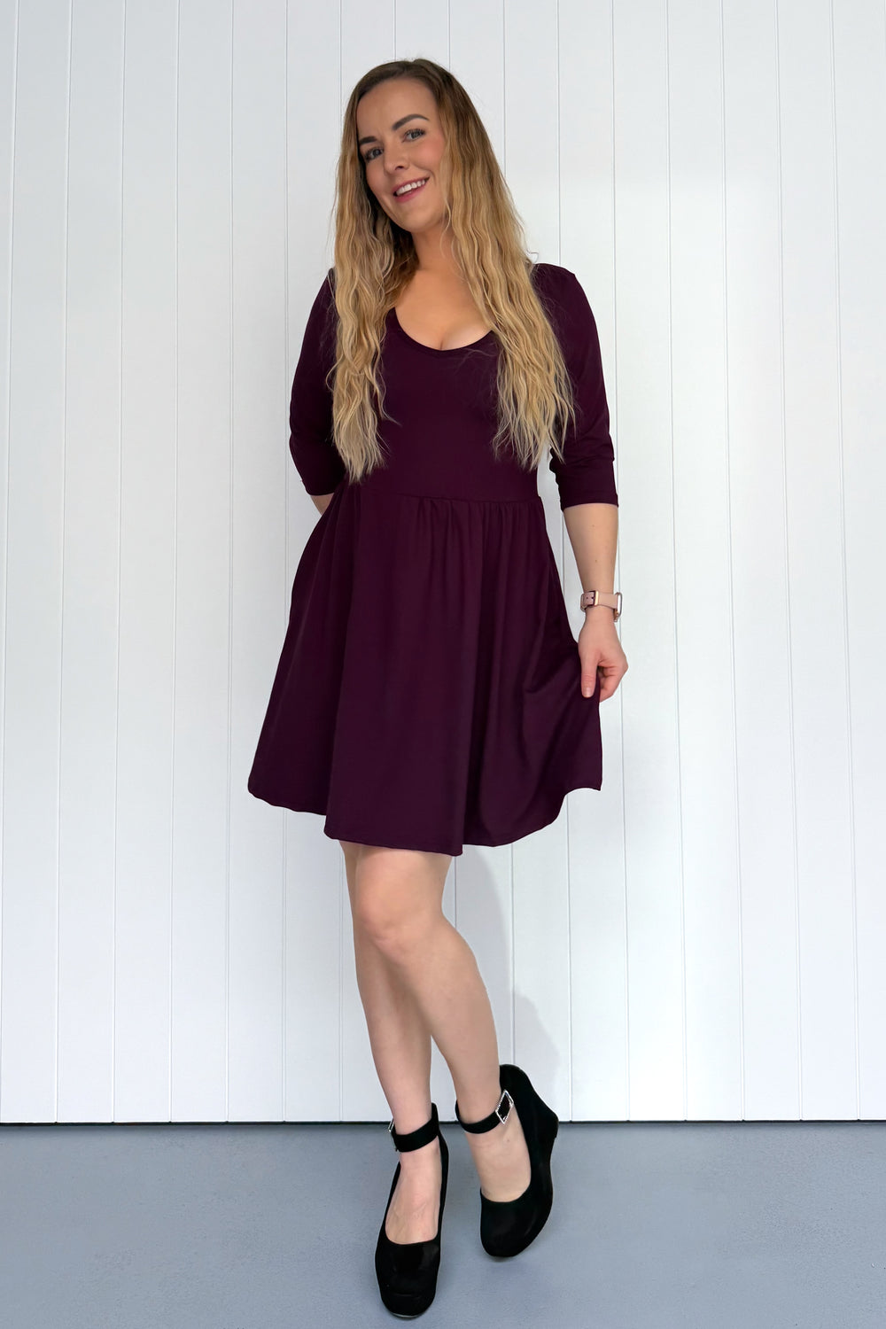 Woman wearing a purple dress standing against a white wall.