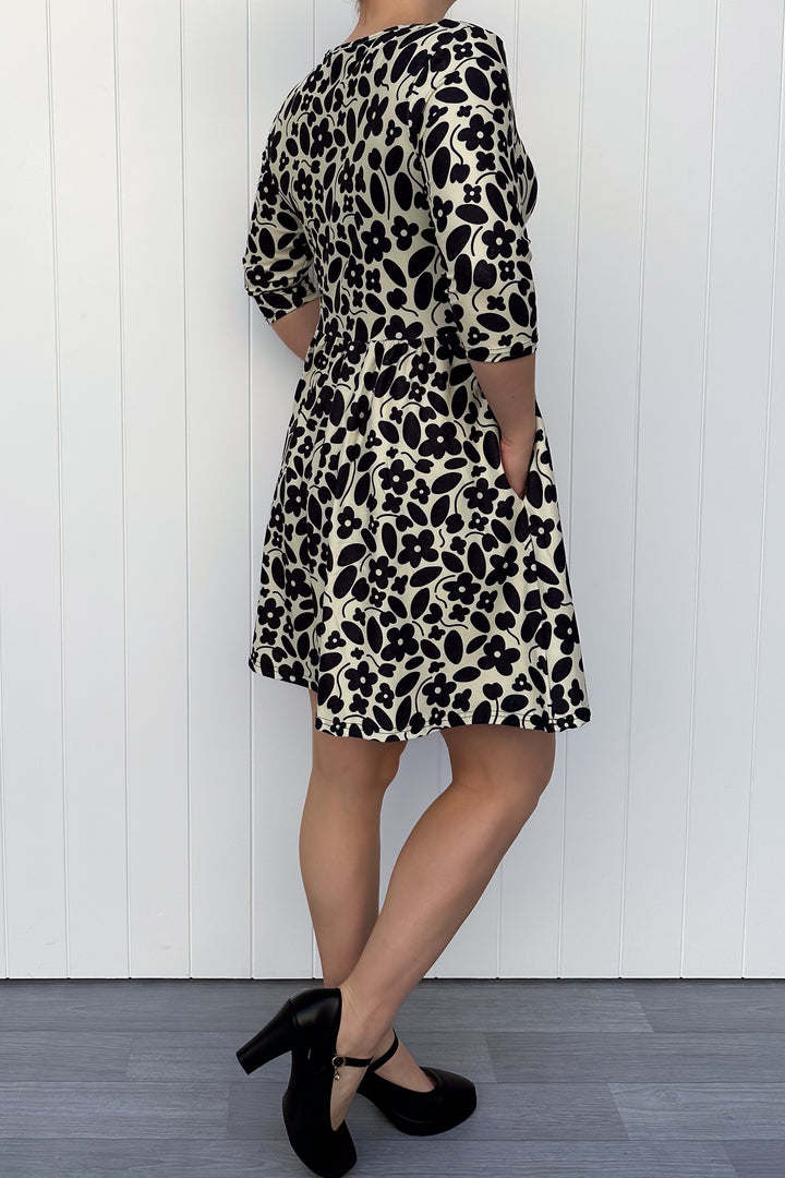 Person wearing a monochrome print dress with flowers and a cream background, against a white wooden panel background