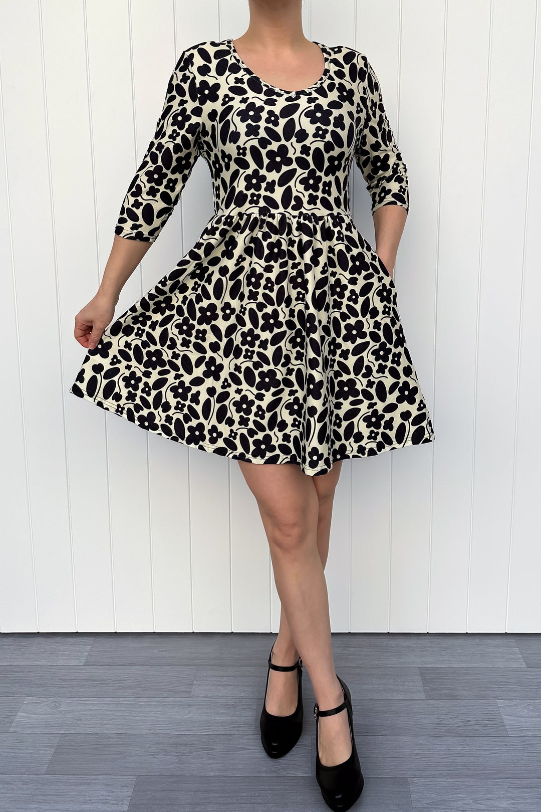 Person wearing a monochrome print dress with flowers and a cream background, against a white wooden panel background