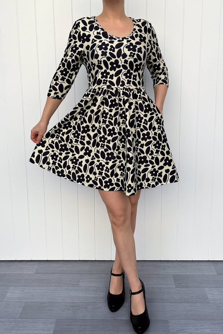 Person wearing a monochrome print dress with flowers and a cream background, against a white wooden panel background