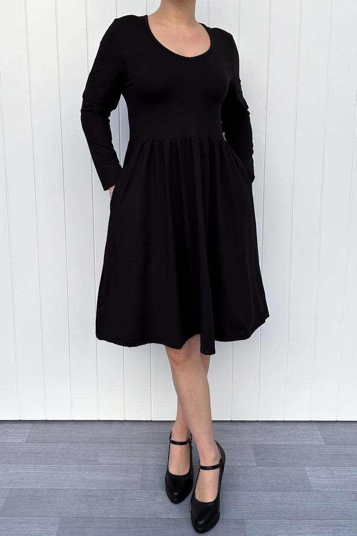 Person wearing a black dress with long sleeves against a white wooden panel background