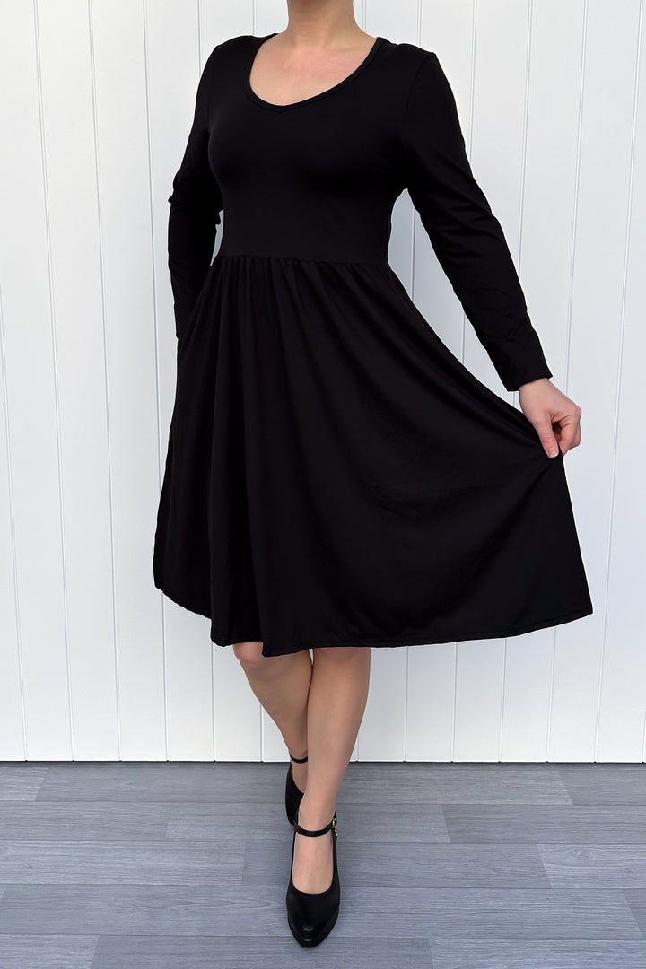 Person wearing a black full sleeve dress against a white wall.