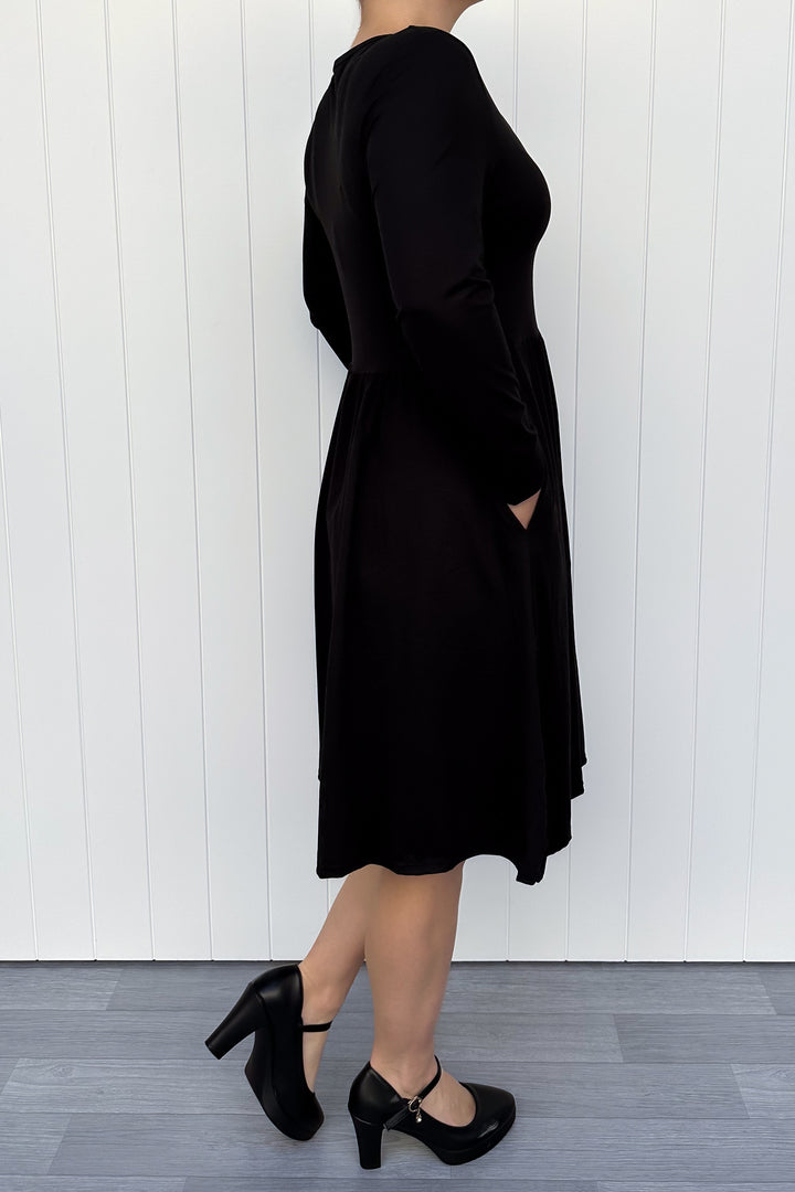 Person wearing a black long sleeve dress against a white wall.
