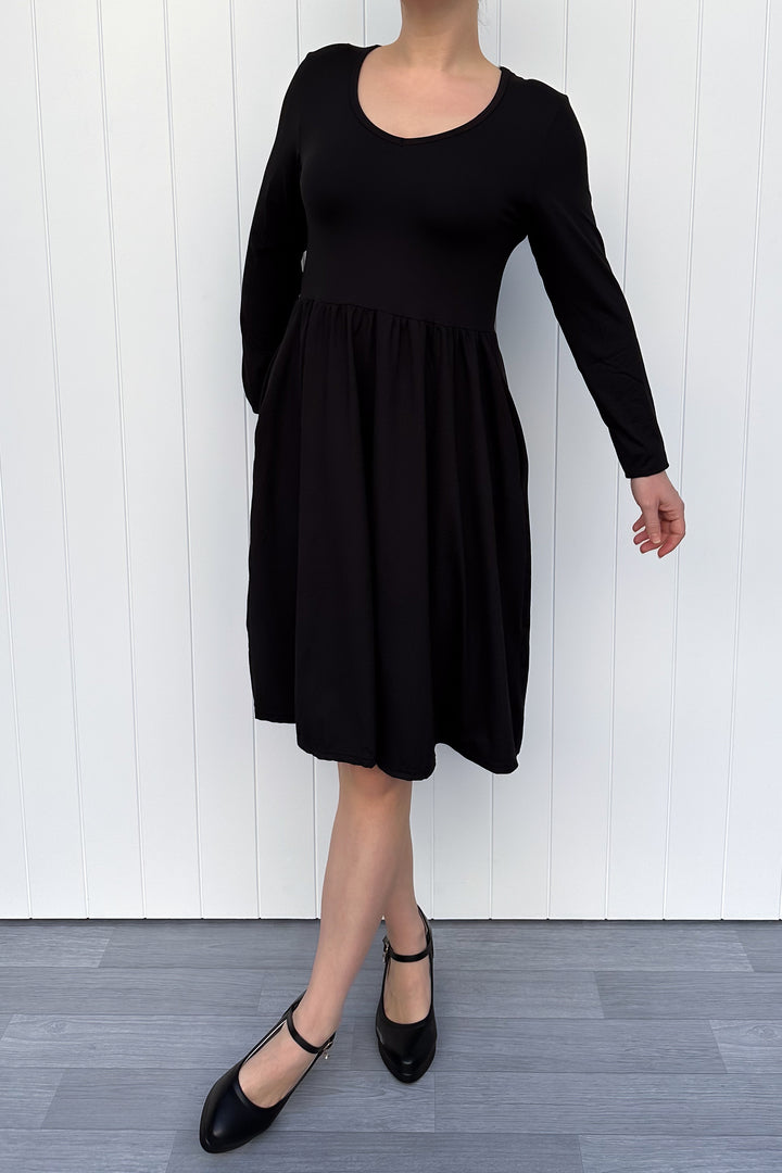 Person wearing a black full sleeve dress against a white wall.