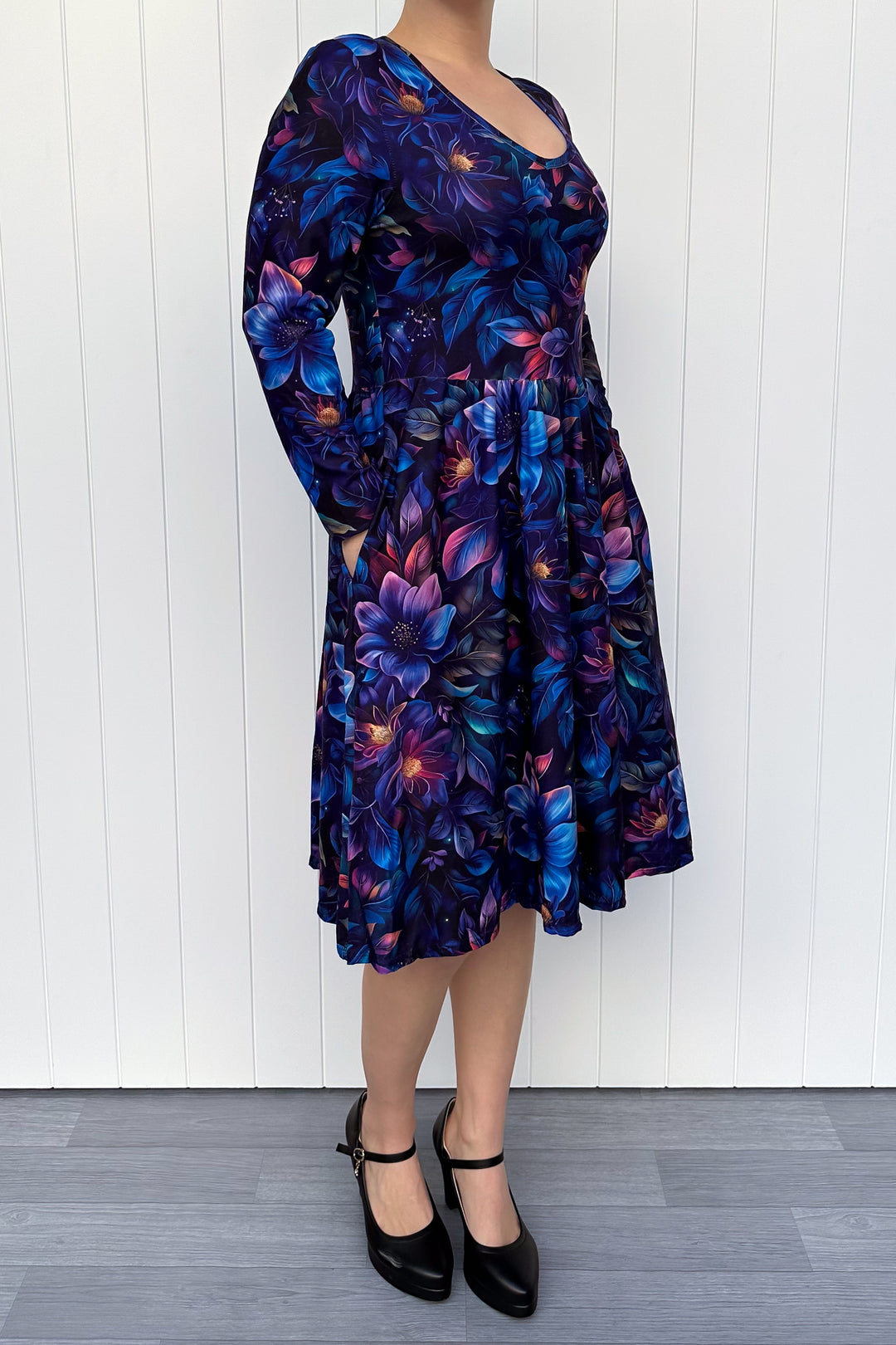 Person wearing a blue floral dress against a white wooden panel background
