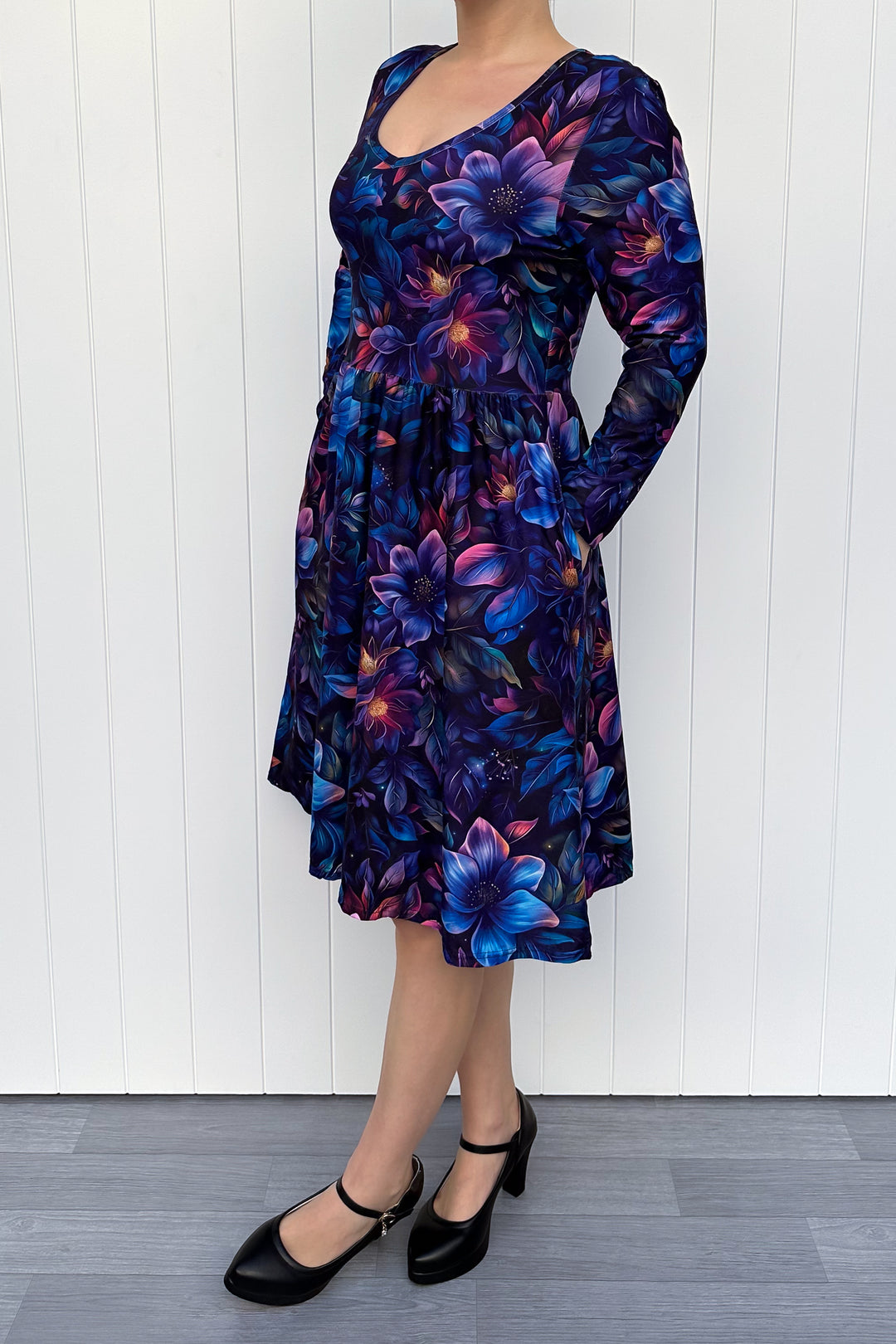 Woman wearing a long-sleeve dress with a blue floral pattern against a white wooden panel background
