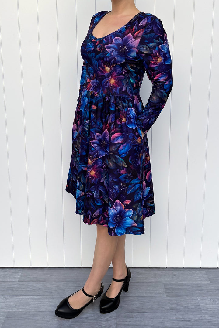 Woman wearing a long-sleeve dress with a blue floral pattern against a white wooden panel background