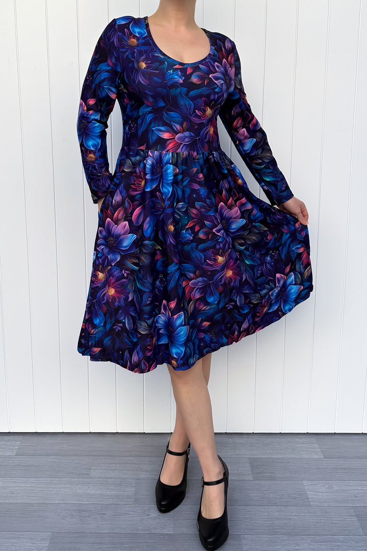 Person wearing a long-sleeve dress with a floral pattern against a white wooden panel background