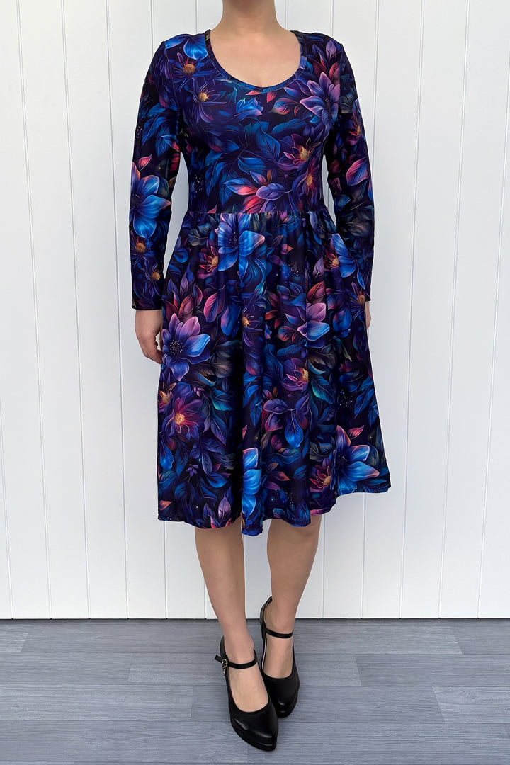 Woman wearing a long-sleeve blue dress with a floral pattern against a white wooden panel background