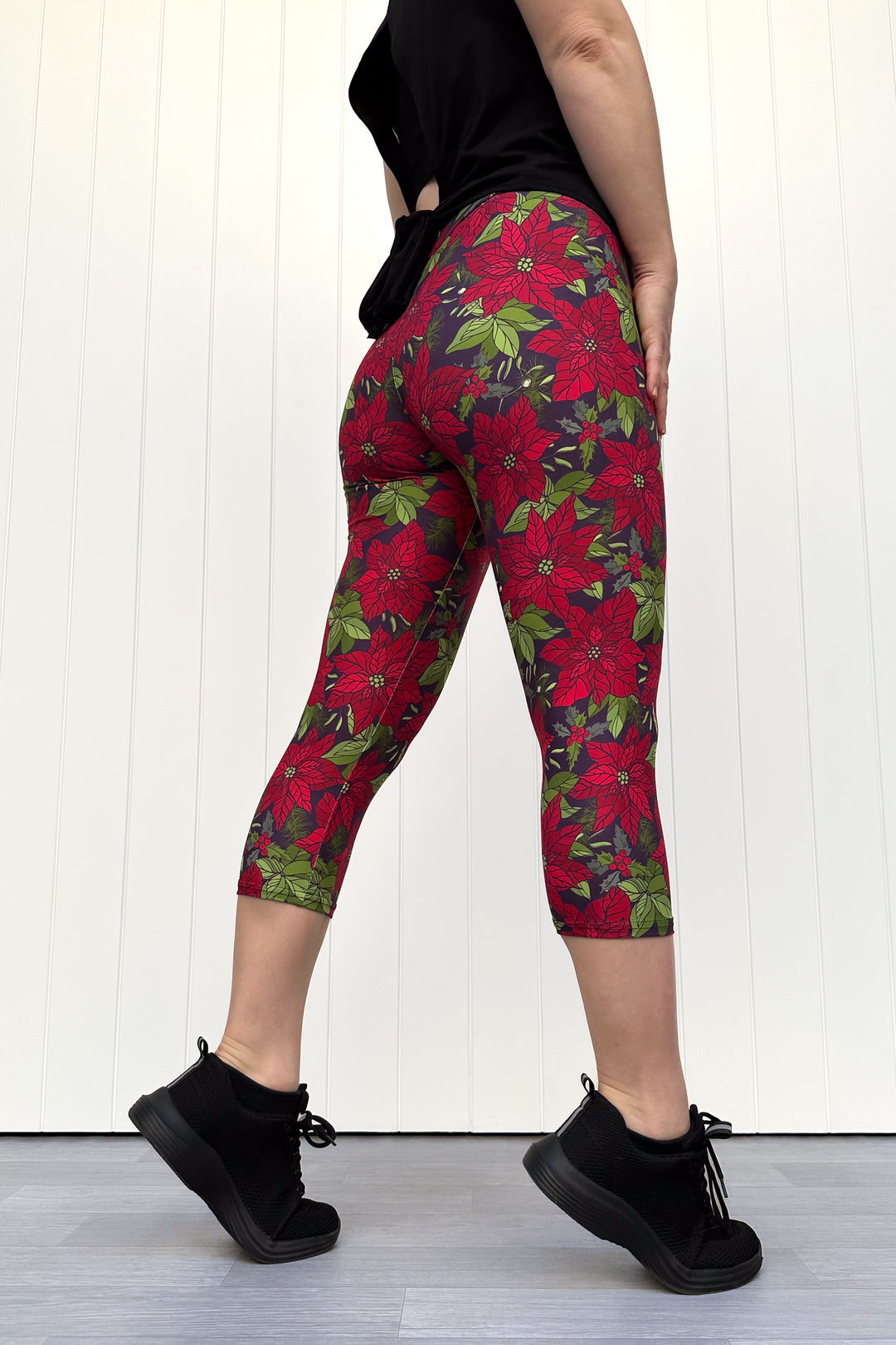 Person wearing red floral Christmas capri leggings, standing against a white wall.
