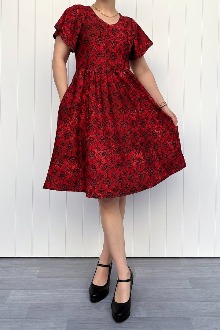 Person wearing a red floral dress against a white wooden panel background