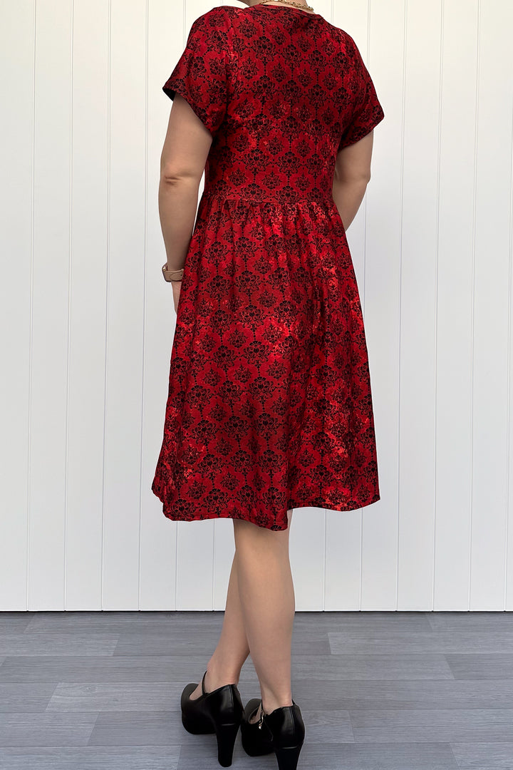 Person wearing a red floral dress against a white wall.
