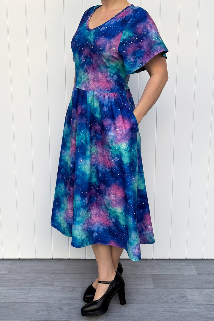 Person wearing a colorful dress with a galaxy pattern against a white wooden panel background