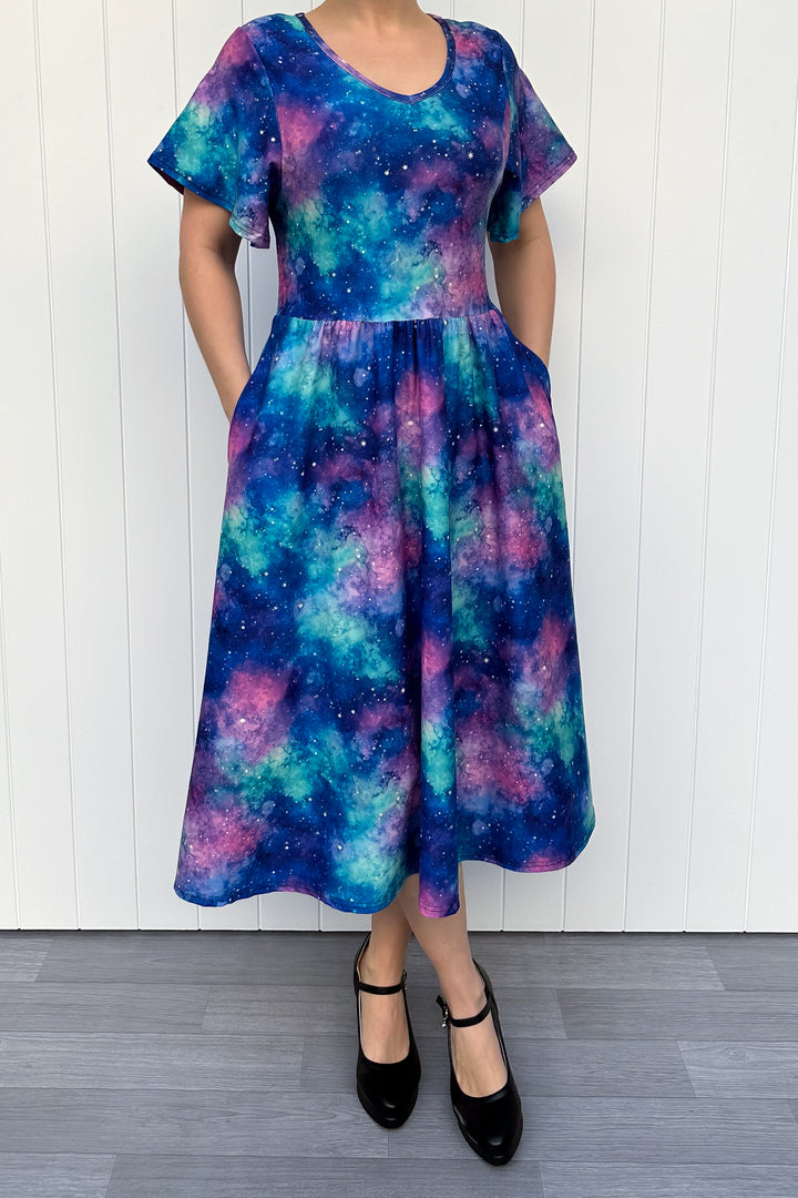 Person wearing a colorful galaxy-patterned dress against a white wooden panel background