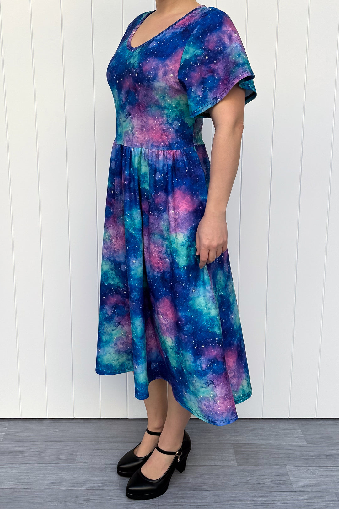 Person wearing a colorful galaxy-patterned dress against a white wooden panel background