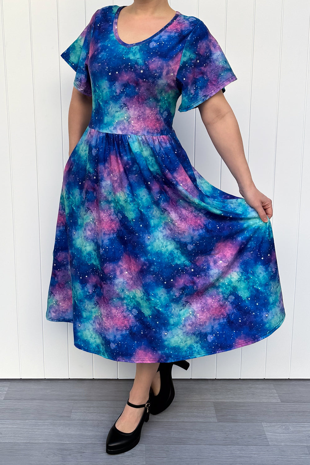 Person wearing a colorful galaxy-patterned dress against a white wall.