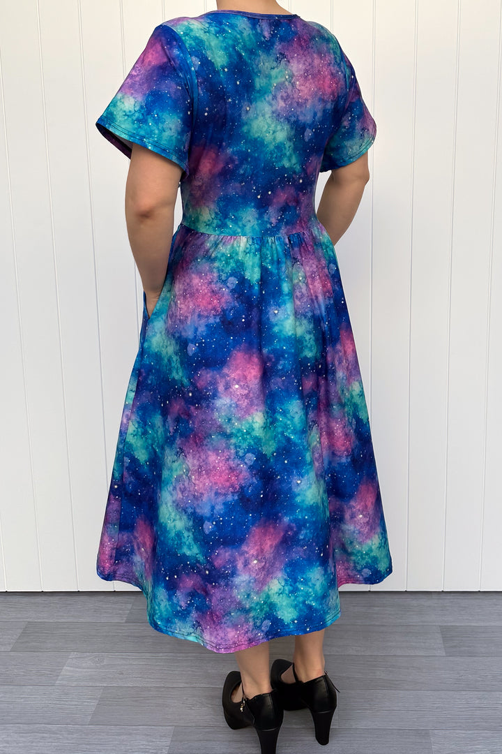 Multicolored galaxy-patterned dress worn by a person against a white wooden panel background.