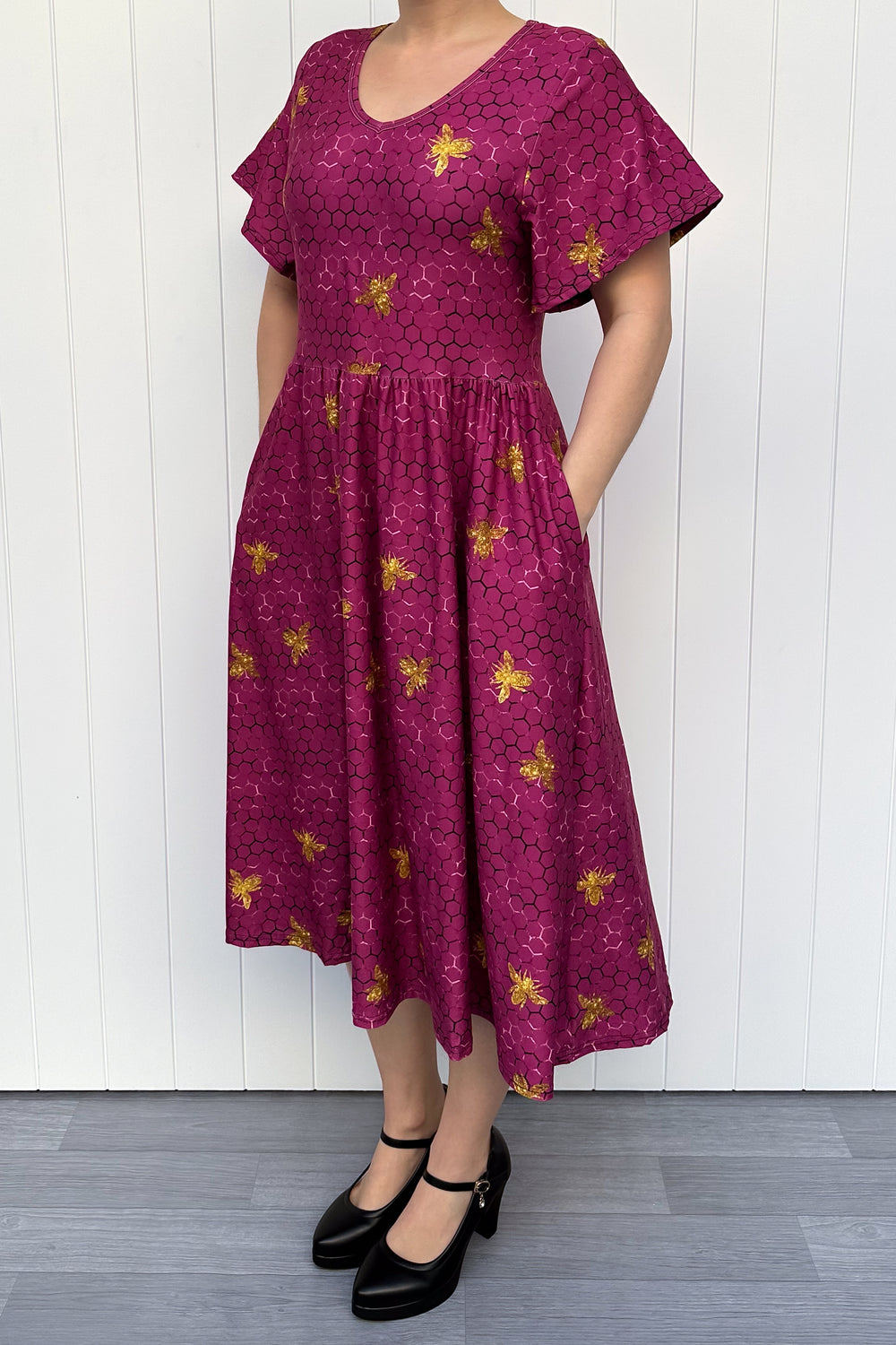Woman wearing a magenta dress with golden bee patterns against a white wooden panel background