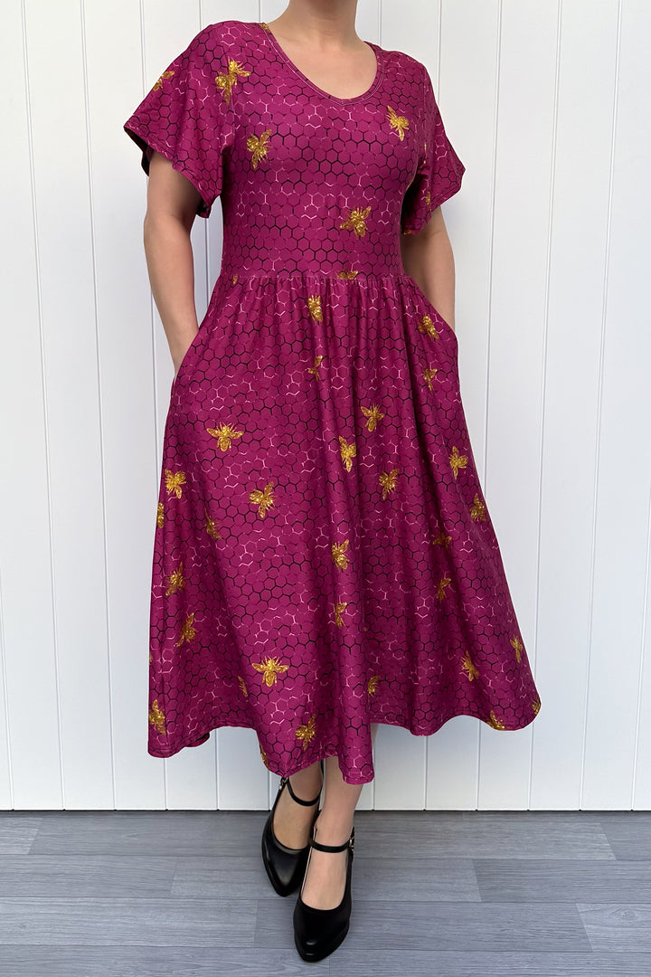 Woman wearing a magenta dress with golden bee patterns against a white wooden panel background