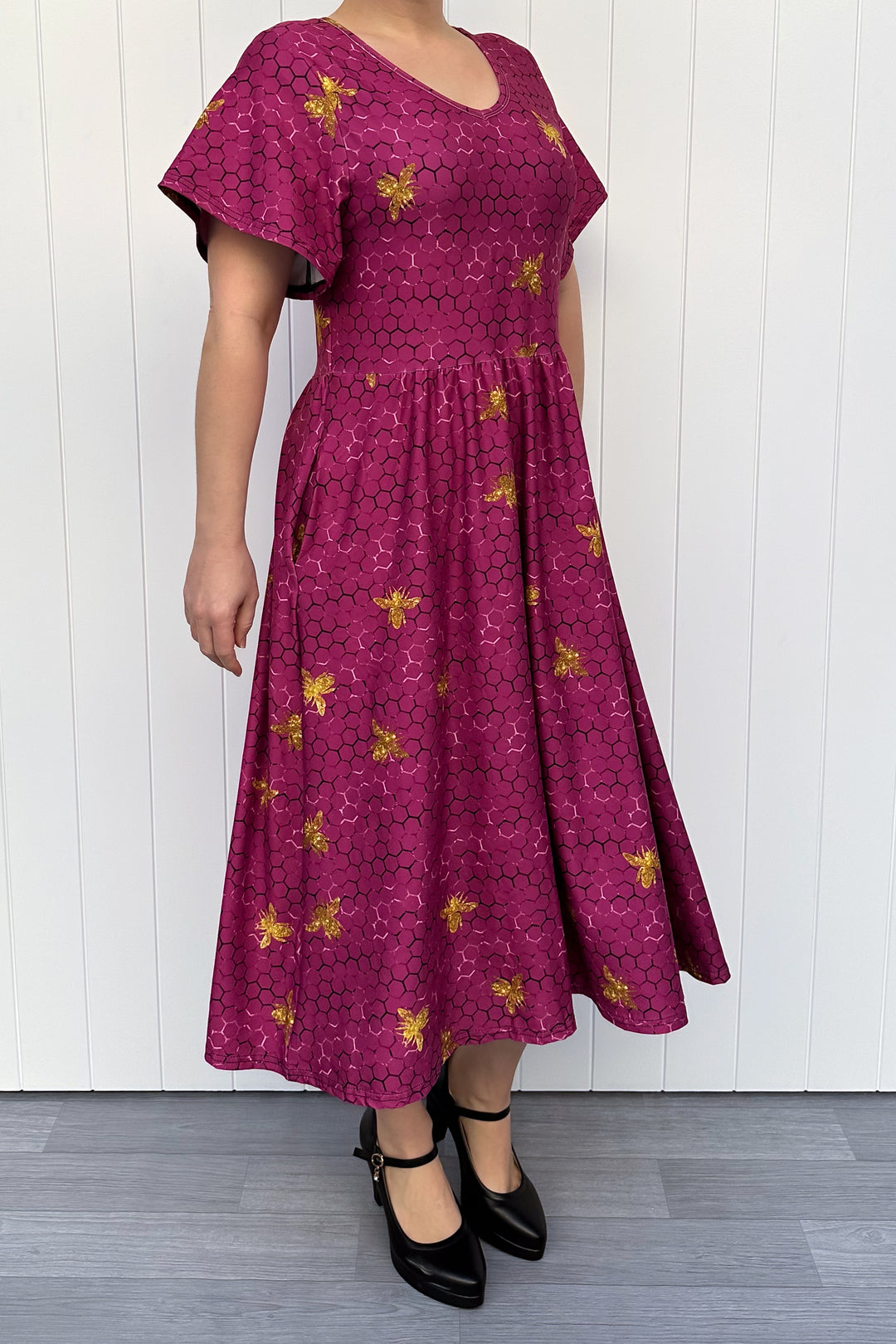 Woman wearing a magenta dress with golden bee patterns against a white wooden panel background