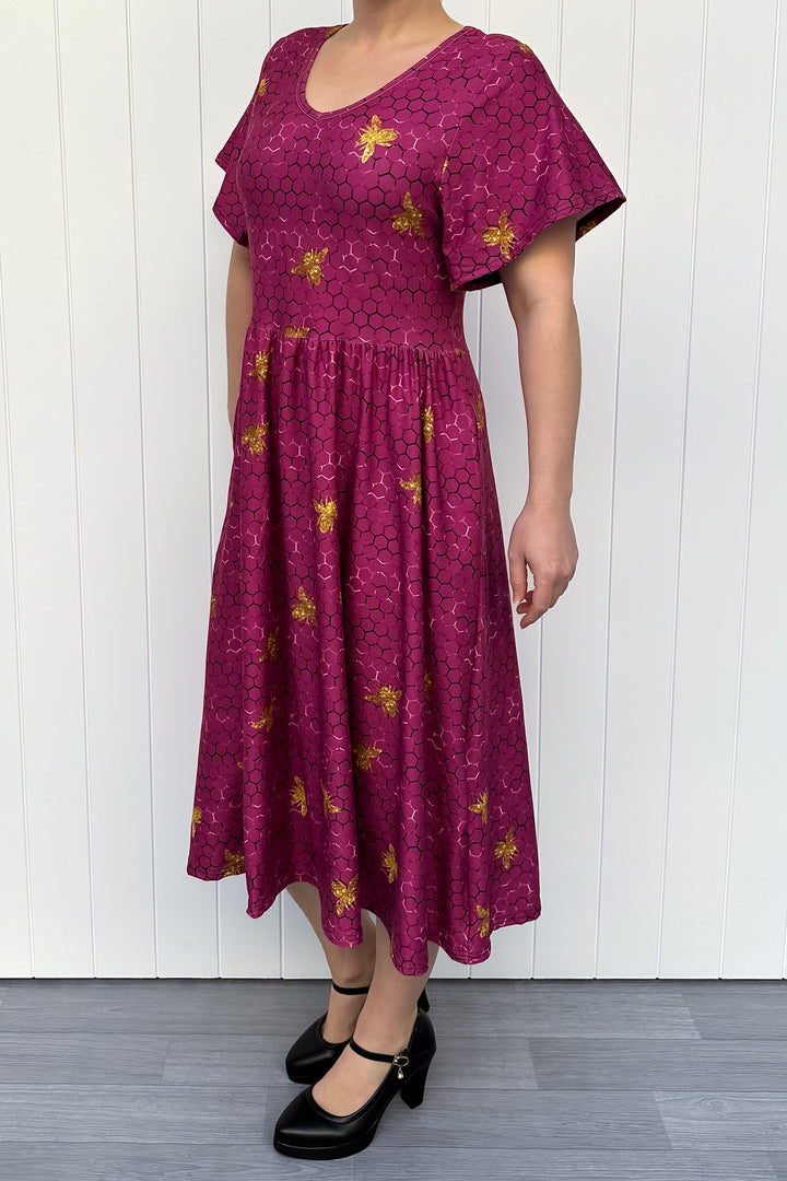 Woman wearing a magenta dress with golden bee patterns against a white wooden panel background