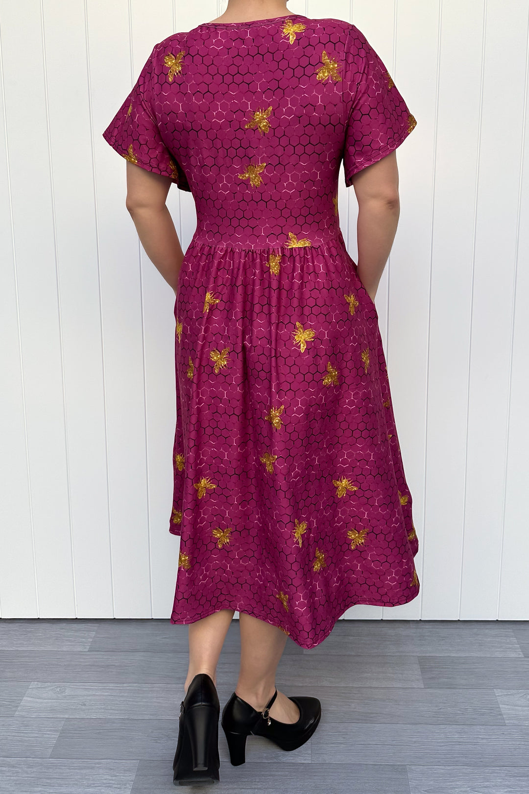 Woman wearing a magenta dress with golden bee patterns against a white wooden panel background