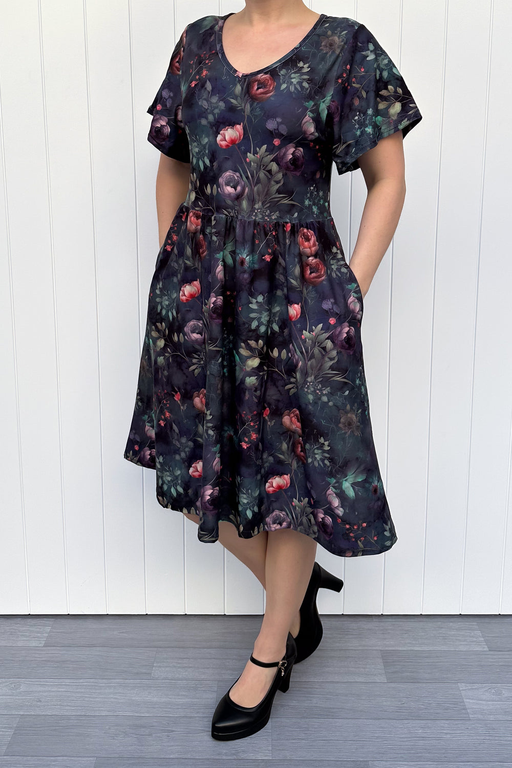 Woman wearing a dark floral dress against a white wooden panel background