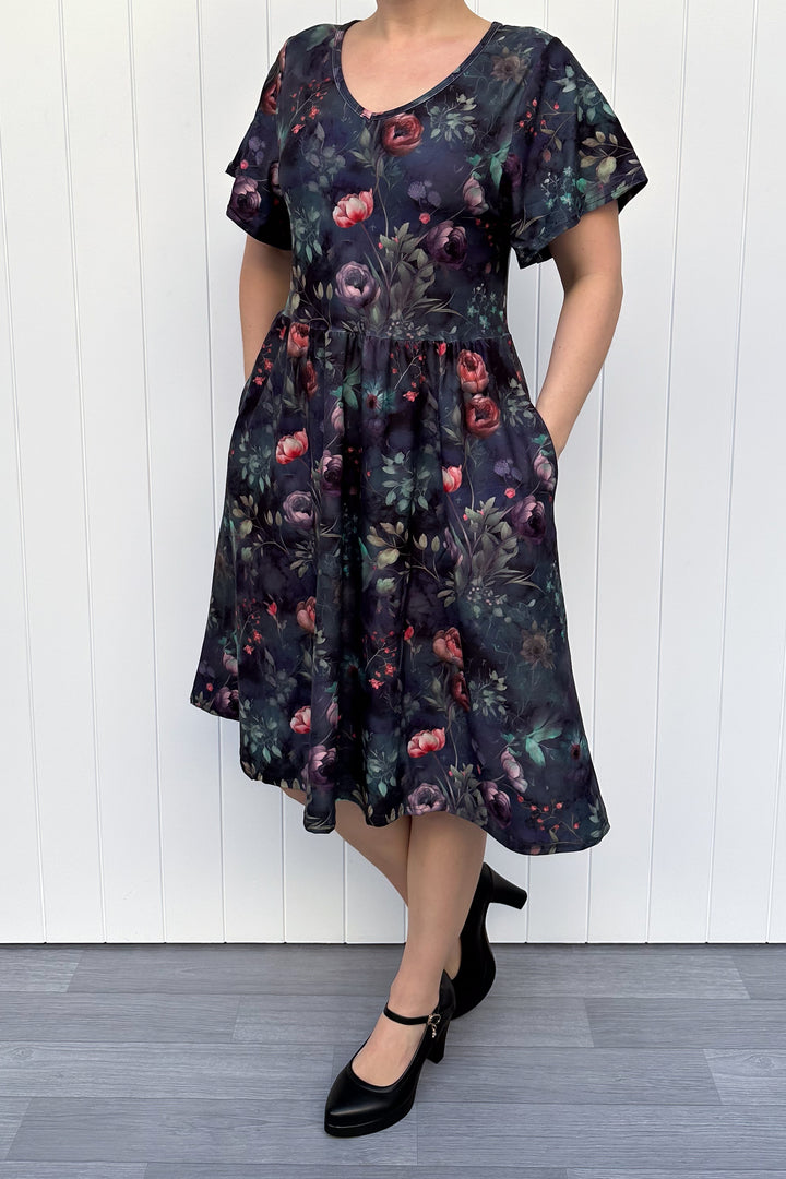 Woman wearing a dark floral dress against a white wooden panel background