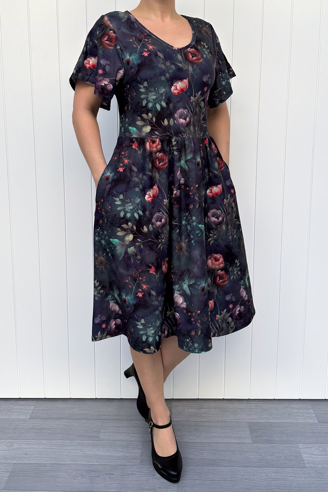 Person wearing a dark floral dress against a white wooden panel background