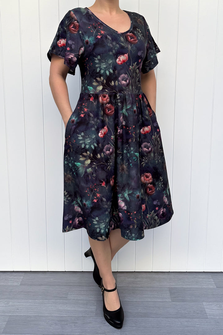 Person wearing a dark floral dress against a white wooden panel background
