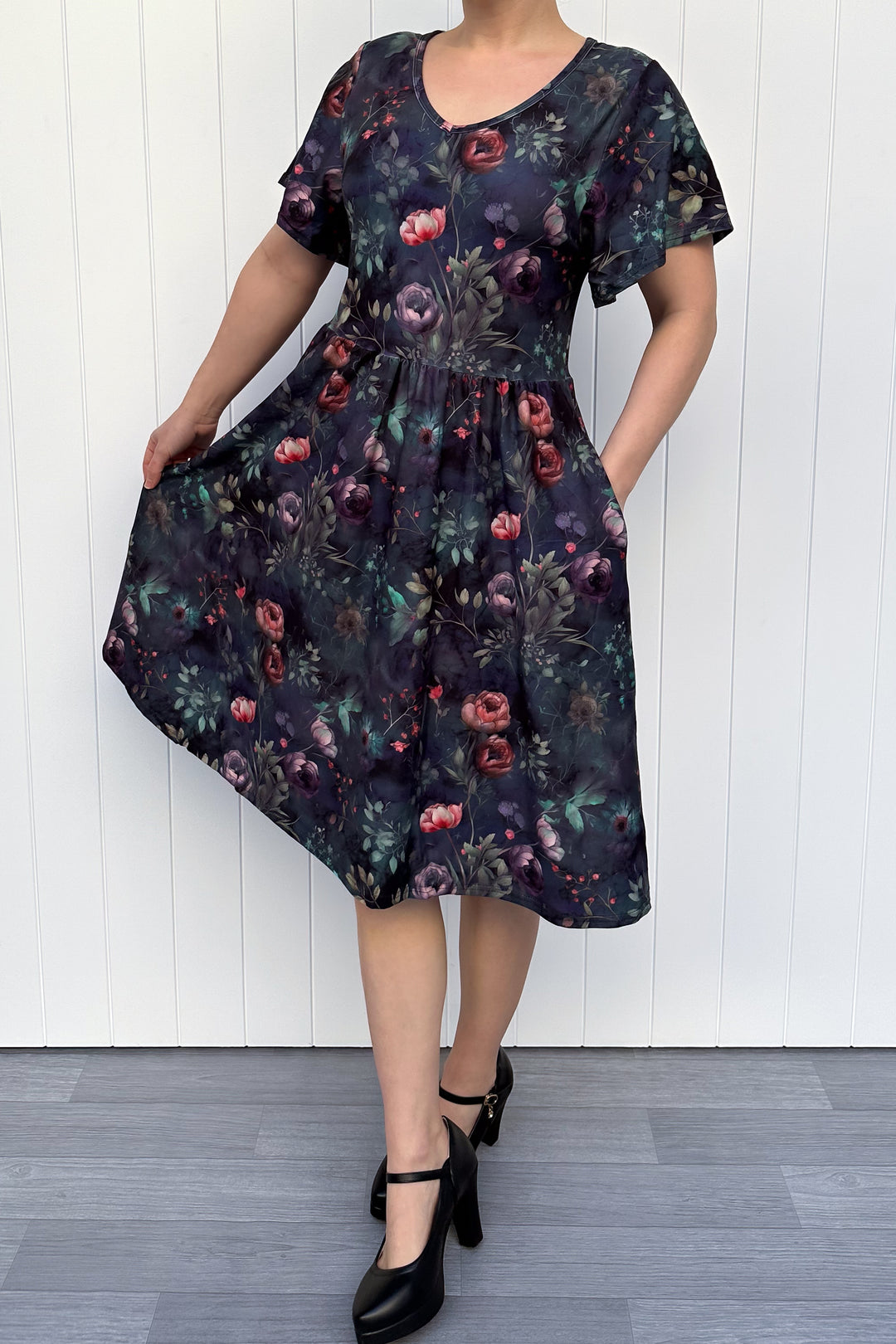 Woman wearing a dark floral dress against a white wooden panel background