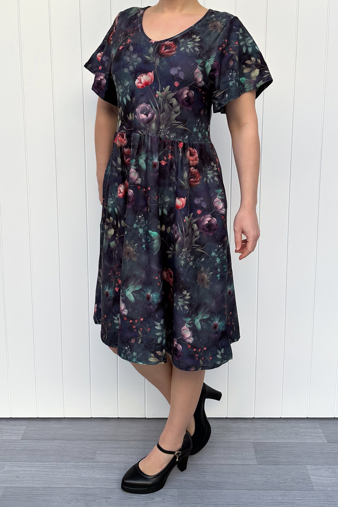 Woman wearing a dark floral dress against a white wooden panel background