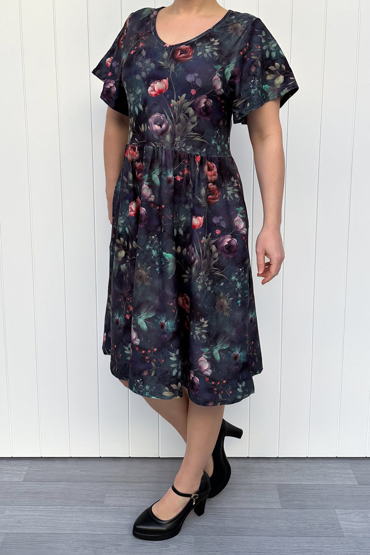 Woman wearing a dark floral dress against a white wooden panel background