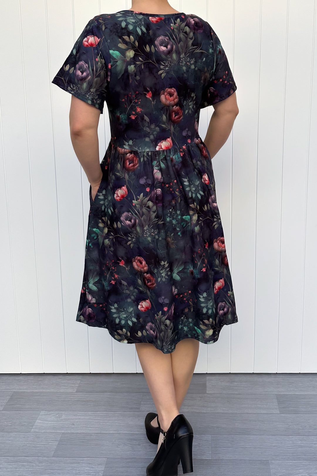 Woman wearing a dark floral dress against a white wooden panel background
