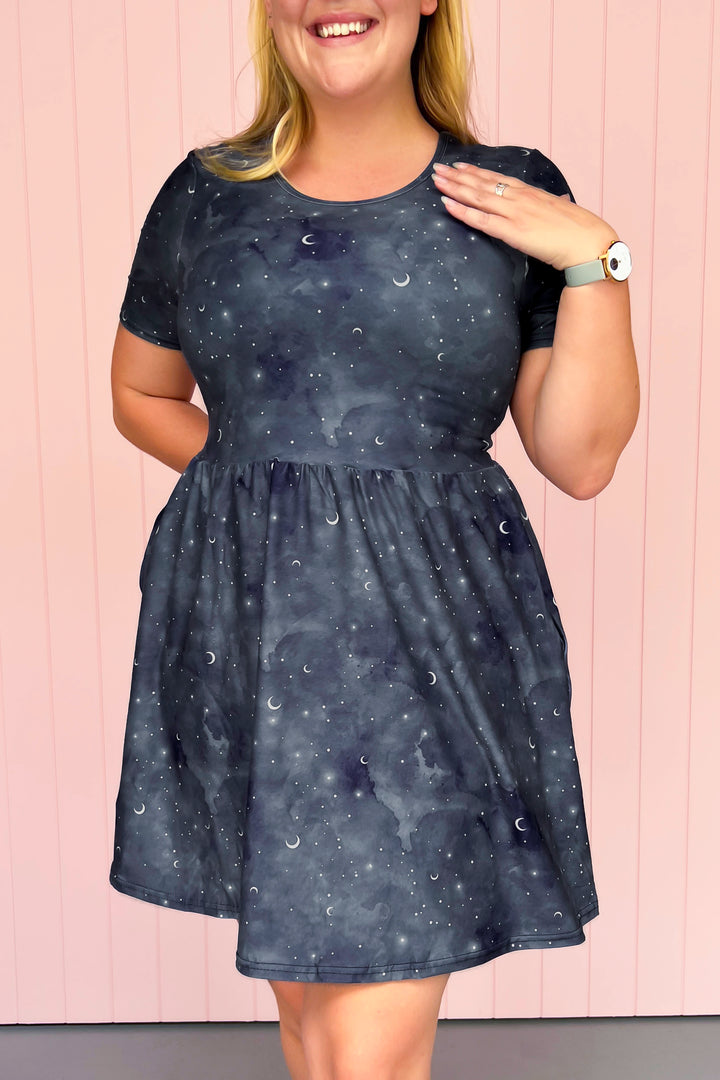 Woman wearing a dark blue dress with celestial pattern against a light pink background