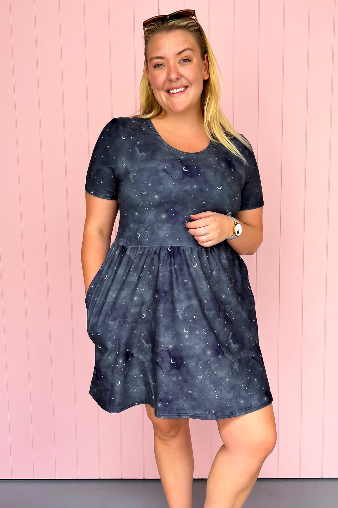 Woman wearing a dark blue dress with celestial pattern against a pink background
